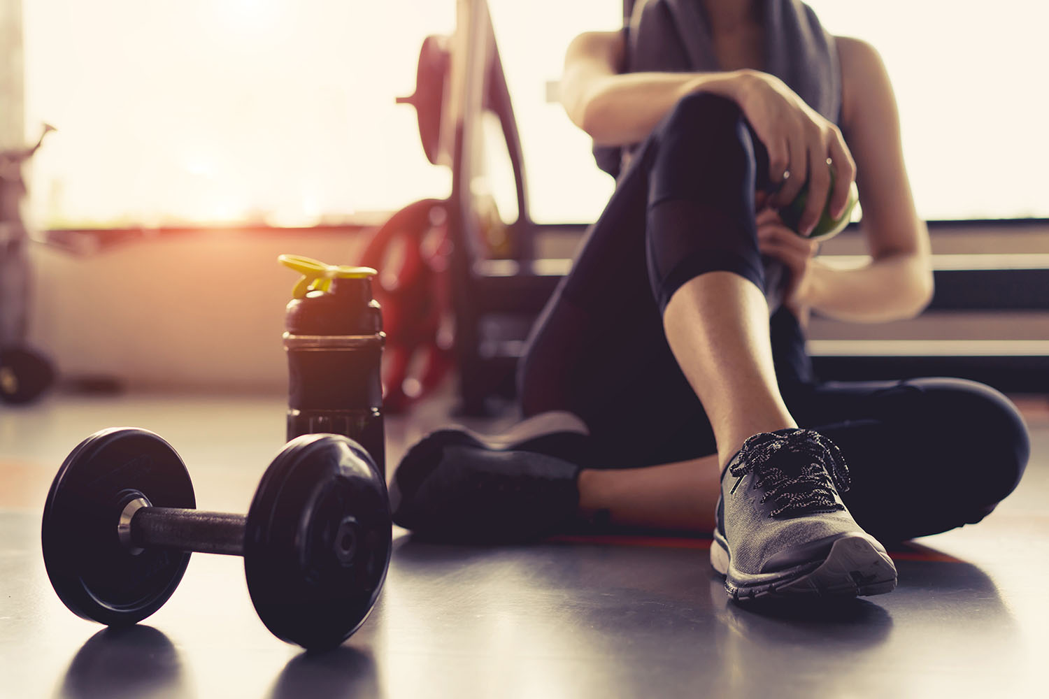 Woman sitting on a gym floor with a dumbell and water bottle beside her